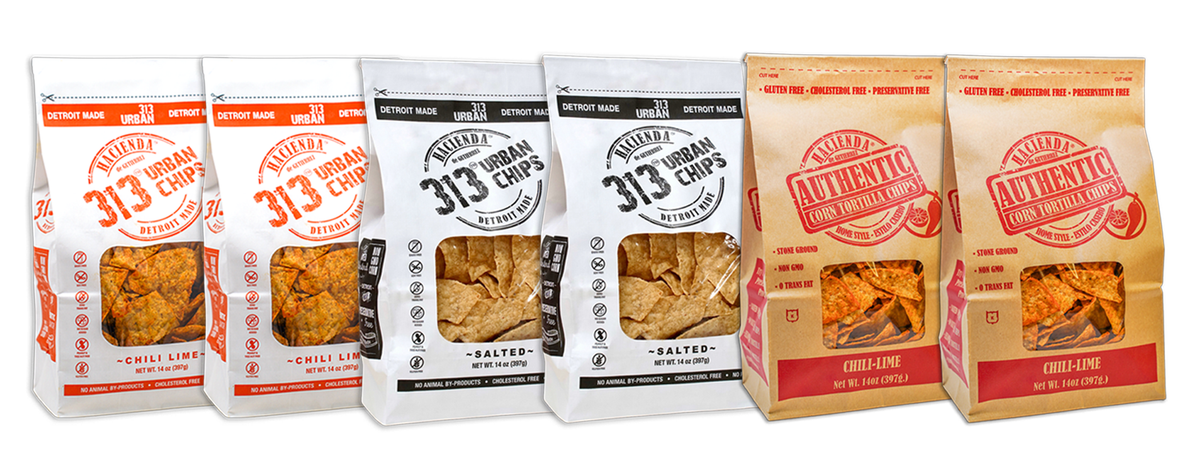 A display of four bags of Hacienda 313 Urban Tortilla Chips and 2 Hacienda Authentic Tortilla Chips. The first two 313 Urban Chips bags are labeled "Chili Lime" with vibrant red labeling. The next two 313 Urban Chips bags are labeled "Salted" in black. The last two Hacienda Authentic tortilla chip bags are labeled "Chili Lime," each bag showcasing a transparent window to view the chips inside, with "DETROIT MADE" printed on the packaging.