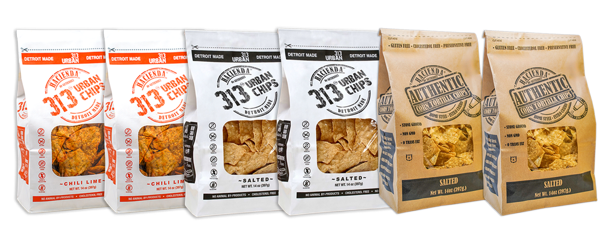 A display of four bags of Hacienda 313 Urban Tortilla Chips and 2 Hacienda Authentic Tortilla Chips. The first two 313 Urban Chips bags are labeled "Chili Lime" with vibrant red labeling. The next two 313 Urban Chips bags are labeled "Salted" in black. The last two Hacienda Authentic tortilla chip bags are labeled "Salted," each bag showcasing a transparent window to view the chips inside, with "DETROIT MADE" printed on the packaging.