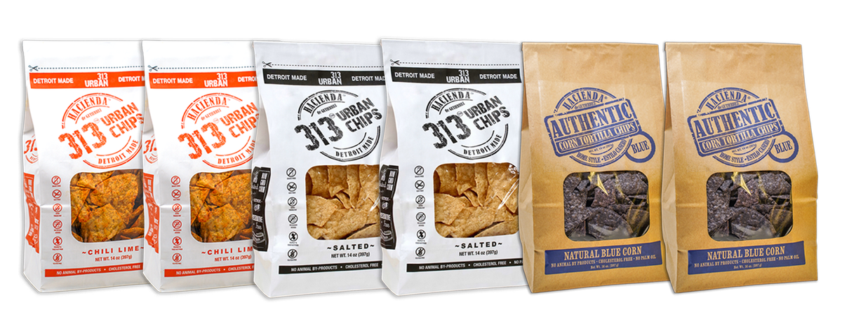 A display of four bags of Hacienda 313 Urban Tortilla Chips and 2 Hacienda Authentic Tortilla Chips. The first two 313 Urban Chips bags are labeled "Chili Lime" with vibrant red labeling. The next two 313 Urban Chips bags are labeled "Salted" in black. The last two Hacienda Authentic tortilla chip bags are labeled "Natural Blue Corn," each bag showcasing a transparent window to view the chips inside, with "DETROIT MADE" printed on the packaging.