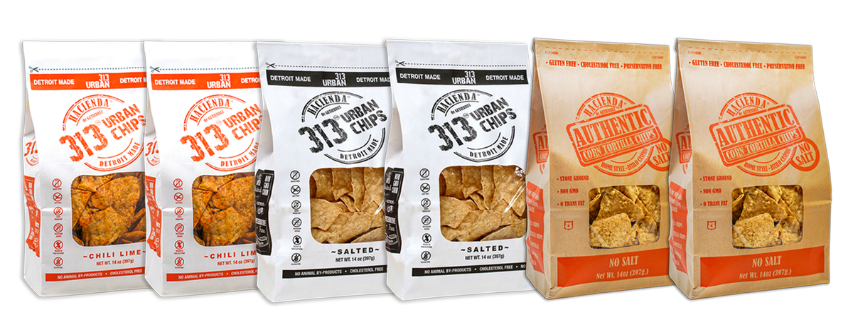 A display of four bags of Hacienda 313 Urban Tortilla Chips and 2 Hacienda Authentic Tortilla Chips. The first two 313 Urban Chips bags are labeled "Chili Lime" with vibrant red labeling. The next two 313 Urban Chips bags are labeled "Salted" in black. The last two Hacienda Authentic tortilla chip bags are labeled "No Salt," each bag showcasing a transparent window to view the chips inside, with "DETROIT MADE" printed on the packaging.