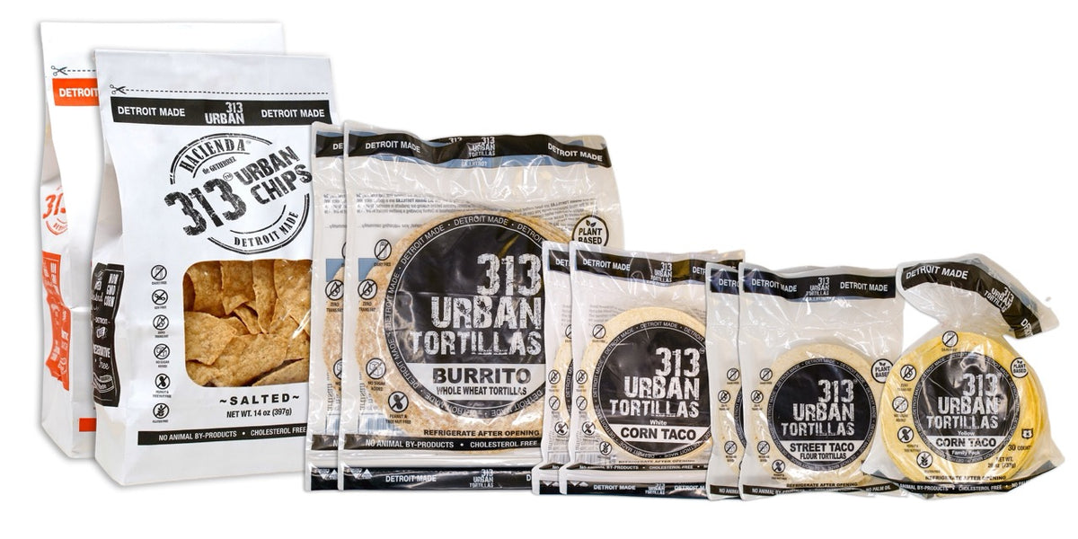 A display featuring several Hacienda 313 Urban products. At the forefront are two bags of tortilla chips, one Salted and the other Chili Lime, labeled &quot;313 Urban Chips&quot;  Behind them are two bags of 8&quot; Whole Wheat tortillas, labeled &quot;313 Urban Tortillas,&quot; followed by two bags of White Corn tortillas, also labeled &quot;313 Urban Tortillas.&quot; Next, there are two bags of 5&quot; Flour tortillas labeled &quot;313 Urban Tortillas,&quot; and finally, a single bag of Yellow Corn tortillas, completing the assortment.