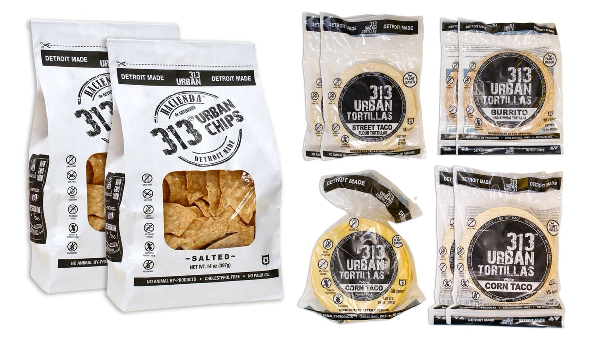 A display featuring several Hacienda products. At the forefront are two bags of 313 Urban Salted tortilla chips, labeled &quot;313 Urban Chips&quot; in a white package with a transparent window to show the chips inside. Behind them are two bags of Street Taco Flour Tortillas, labeled &quot;313 Urban Tortillas.&quot; Next, there are two bags of Burrito tortillas, which are Whole Wheat 313 Urban Tortillas, and finally, two bags of White Corn 313 Urban Tortillas. All bags prominently display &quot;DETROIT MADE&quot; on the packaging.