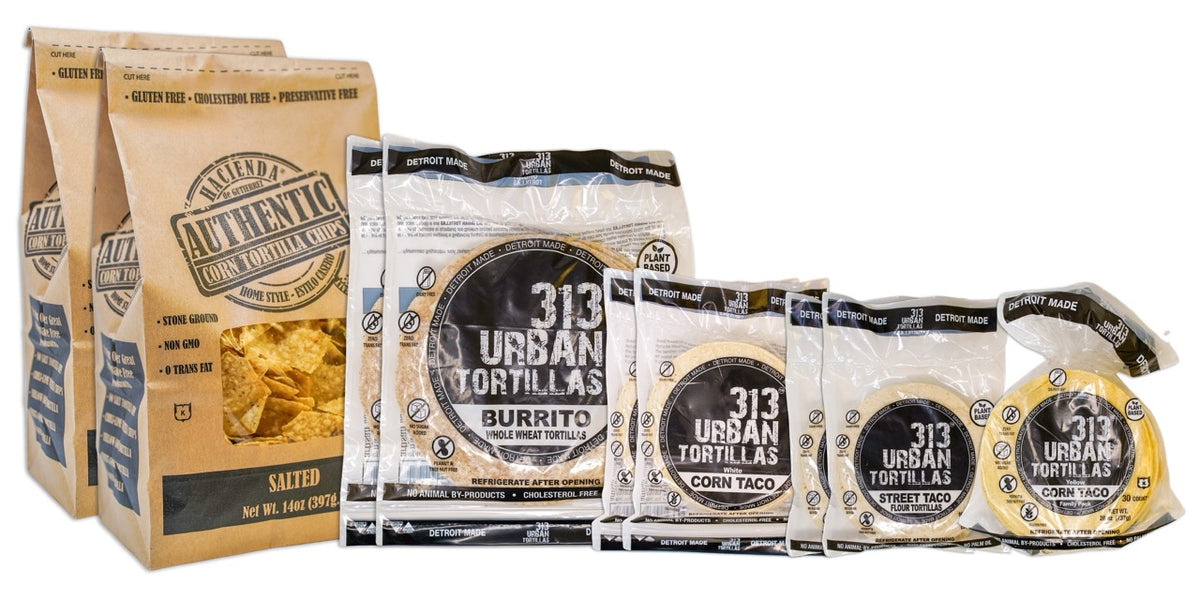 A display featuring several Hacienda products. At the forefront are two bags of Authentic Salted tortilla chips, labeled &quot;Hacienda Authentic Corn Tortilla Chips&quot; in brown packaging. Behind them are two bags of 8&quot; Whole Wheat 313 Urban Tortillas, followed by two bags of White Corn 313 Urban Tortillas. Next, there are two bags of 5&quot; Flour 313 Urban Tortillas, and finally, a single bag of Yellow Corn 313 Urban Tortillas. All bags prominently feature &quot;DETROIT MADE&quot; on the packaging.